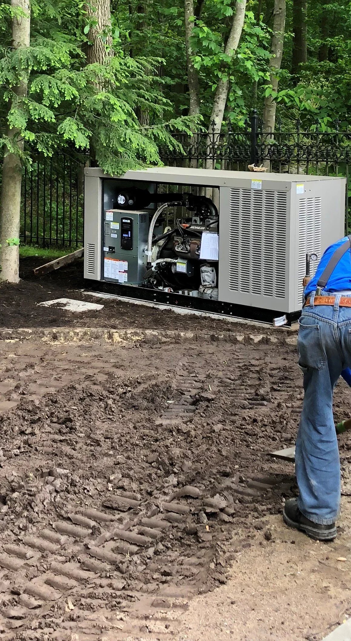 Sixty kilowatt standby generator on a concrete pad with technician working at the enclosure